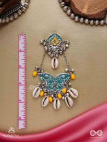 SHANKHA PUSHPA- CONCH BLOSSOM-OXIDIZED EARRINGS WITH PASTEL-HUED METALWORK, EMBELLISHED WITH DELICATE COWRIE SHELLS, YELLOW BEADS AND GHUNGROO