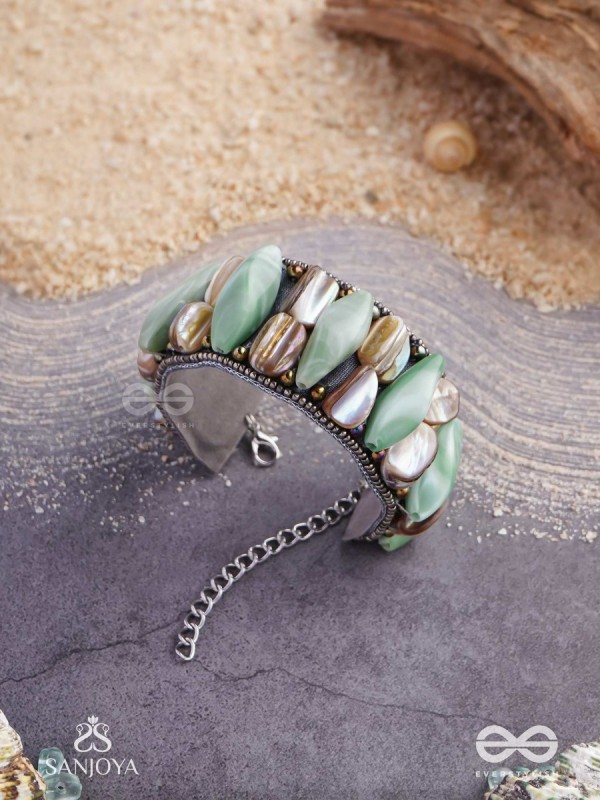 Shuktimālā- Shell band-Expandable bracelet crafted from shell beads, combining turquoise and beige-brown tones with a brassy finish.