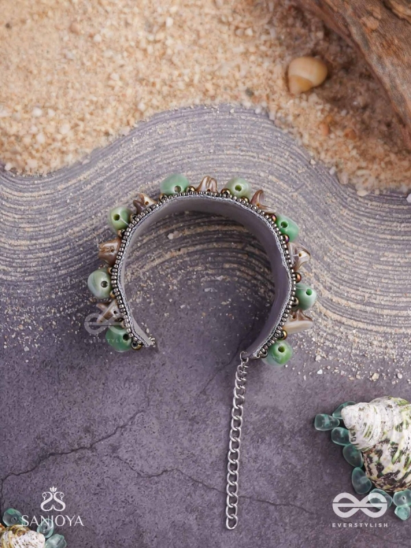 Shuktimālā- Shell band-Expandable bracelet crafted from shell beads, combining turquoise and beige-brown tones with a brassy finish.