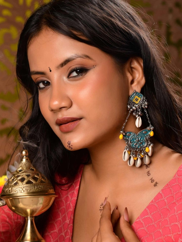 SHANKHA PUSHPA- CONCH BLOSSOM-OXIDIZED EARRINGS WITH PASTEL-HUED METALWORK, EMBELLISHED WITH DELICATE COWRIE SHELLS, YELLOW BEADS AND GHUNGROO