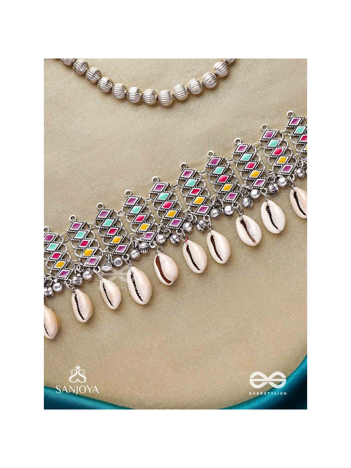 SHANKHAMALA-CONCH GARLAND- OXIDIZED NECKPIECE FEATURING PASTEL-COLOURED METALWORK, EMBELLISHED WITH DANGLING COWRIE SHELLS AND GHUNGROO'S