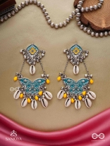 SHANKHA PUSHPA- CONCH BLOSSOM-OXIDIZED EARRINGS WITH PASTEL-HUED METALWORK, EMBELLISHED WITH DELICATE COWRIE SHELLS, YELLOW BEADS AND GHUNGROO