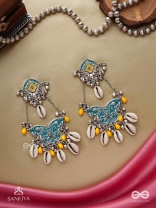 SHANKHA PUSHPA- CONCH BLOSSOM-OXIDIZED EARRINGS WITH PASTEL-HUED METALWORK, EMBELLISHED WITH DELICATE COWRIE SHELLS, YELLOW BEADS AND GHUNGROO